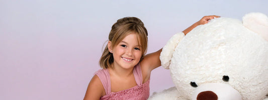 Mädchen mit frisch gestochenen Ohrringen sitzt lächelnd mit weißem Teddybär bei Juwelier Vorarlberg